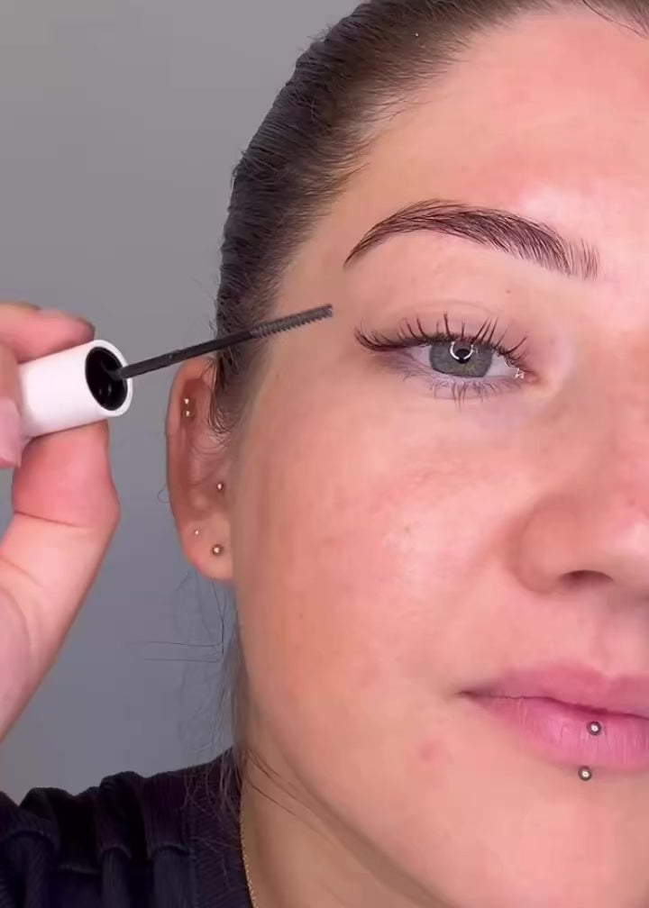 up close video of girl applying a clear mascara through her lashes on a grey background