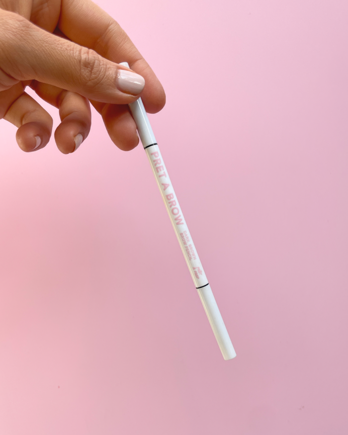 hand holding white eyebrow pencil on pink background