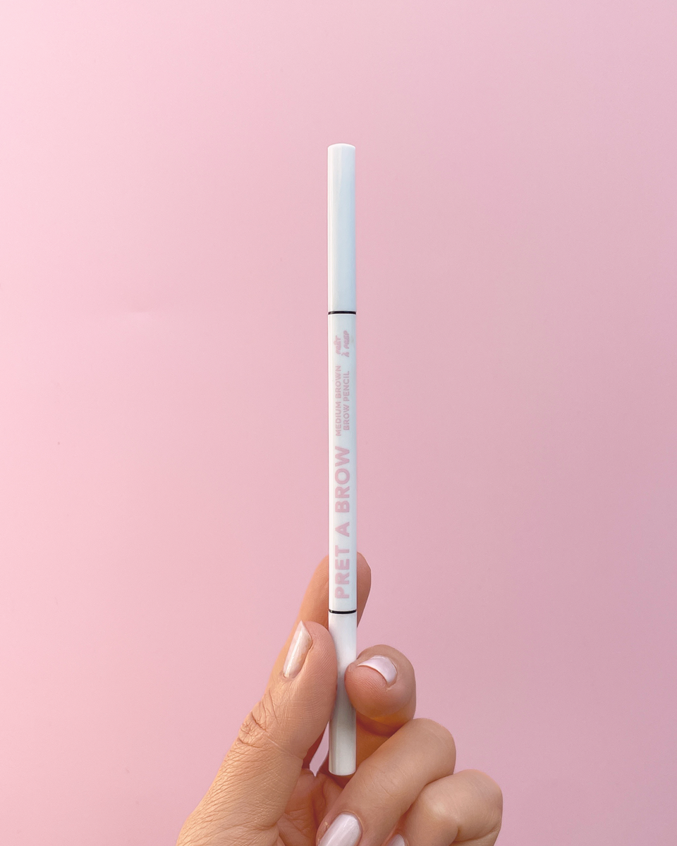 hand holding white eyebrow pencil on pink background